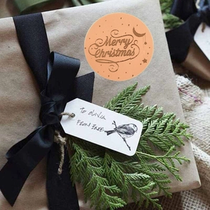 Roll of gold-stamped Merry Christmas stickers on a gift box with warm festive decor