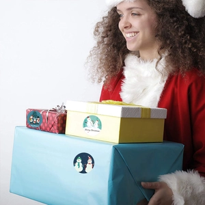 Weihnachtsaufkleber auf Geschenkboxen, gehalten von einer Frau in Festtagsmode