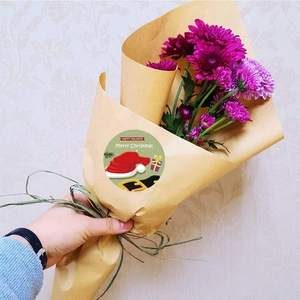Gros plan d'autocollants Joyeux Noël sur un bouquet de fleurs emballé dans du papier kraft
