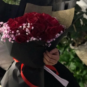 Black kraft paper wrapping for red roses bouquet with decorative gold accent and red ribbon