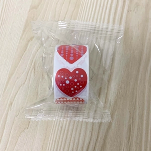 Detail of heart pattern sticker roll in plastic wrap on light wood background