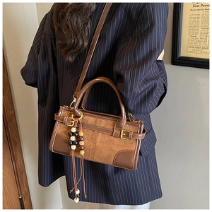 Detail of retro brown baguette bag with suede texture and wooden bead charm on a model