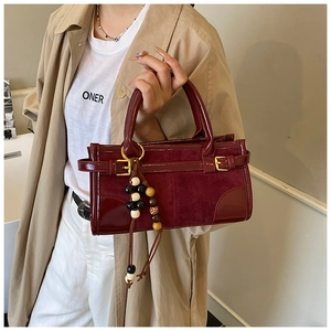Detail of burgundy patchwork shoulder bag with suede texture and beaded charm pendant