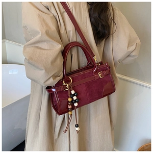 Detail of burgundy baguette bag with mixed textures, beaded charm, and metallic buckle