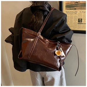 Detail of dark brown patent leather tote bag with baseball pendant on shoulder