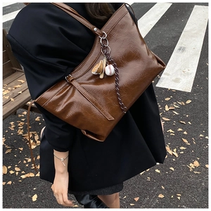 Detail of dark brown tote bag with glossy leather texture and baseball charms on a shoulder strap