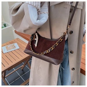 Détail du sac seau marron en daim et cuir avec chaîne dorée et pompon perlé décoratif