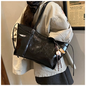 Detail view of black patent leather tote bag with crinkle texture and baseball charm