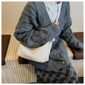 Detail of white pleated texture shoulder bag styled with a grey knit cardigan and skirt