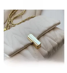 Detail view of beige quilted handbag featuring gold twist lock and chain strap