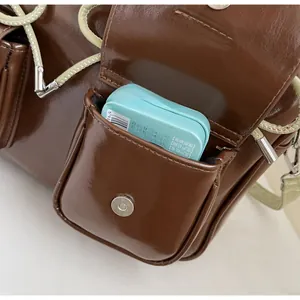 Detail of glossy brown handbag featuring a functional side pocket and woven shoulder strap