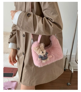 Detail der rosa Plüsch-Umhängetasche mit Bärenanhänger auf einem beigen Trenchcoat