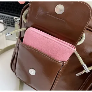 Detail showing front pocket capacity of brown glossy leather shoulder bag with pink pouch