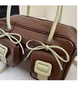 Detail view of brown glossy Boston bag with green bows and front flap pockets