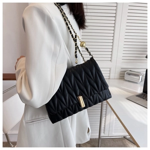 Detail of black quilted leather crossbody bag with golden chain strap and ball ornament