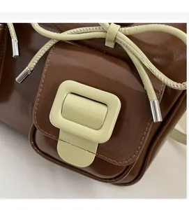 Detail of coffee brown glossy faux leather bag with green decorative buckle and woven cord