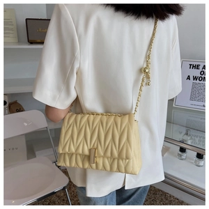 Detail showing creamy quilted crossbody bag with gold chain strap on a model