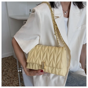 Detail of light yellow quilted crossbody bag with gold chain strap and metal clasp closure