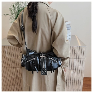 Detail of black punk motorcycle shoulder bag with silver zippers on a beige trench coat