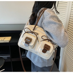 Close-up of cream shoulder bag featuring brown leather buckles and bow ties details