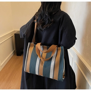 Rear view of a large striped canvas tote bag with brown straps worn by a model