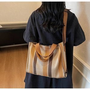 Detail of striped canvas tote bag with brown straps shown on shoulder in interior setting