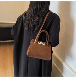 Detail of a brown suede handbag with golden metal clasp worn with a black coat