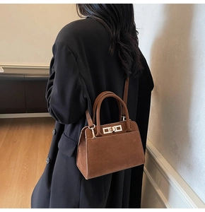 Detail of a brown suede handbag showing the golden twist lock and top handle texture
