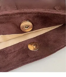 Detail of golden magnetic clasp with textured finish on brown suede tote bag