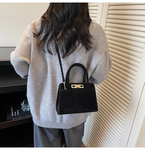 Detail view of black suede shoulder bag with golden twist lock and slim strap for women
