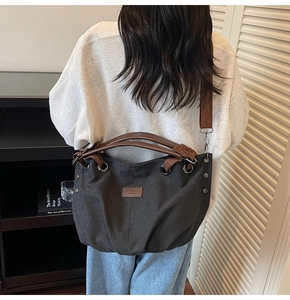 Detail of grey canvas tote bag with brown leather handles and adjustable woven strap