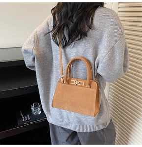 Detailed close-up of brown suede crossbody bag with golden metal buckle and top handles