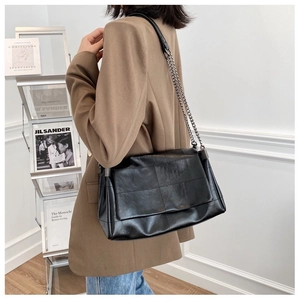 Side view of a black quilted leather shoulder bag with silver chain strap worn by a model