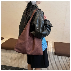 Detail view of large dark brown suede tote bag worn on shoulder in minimalist setting