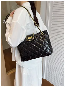 Detail of black quilted tote bag with golden chain strap and woven leather edges