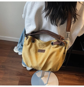 Detail of yellow canvas tote bag with brown leather handles and adjustable shoulder strap