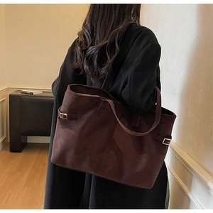Brown suede tote bag side view with metal buckle and dual straps on model's shoulder
