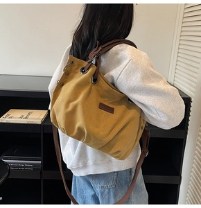 Detail of yellow canvas tote bag featuring brown leather handles and adjustable shoulder strap