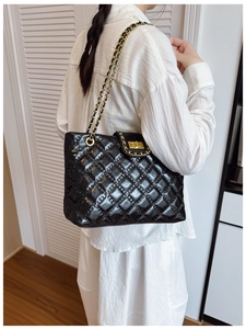 Detail of black quilted patent leather tote bag with gold metal twist lock and chain strap