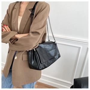 Detail of a black quilted shoulder bag with chain strap worn by a model in casual attire