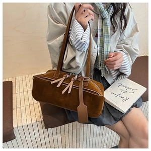 Close-up of a dark brown suede shoulder bag with dual zippers and leather tassel details