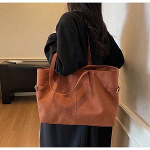 Detail of tan suede tote bag showing side metal buckles and soft texture on model