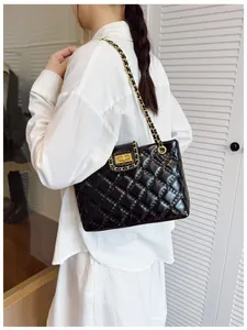 Detail of black quilted tote bag with gold chain strap and metal lock shown on model