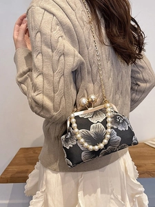 Sac à main brodé vintage avec fermoir perle et bandoulière sur un pull en maille beige