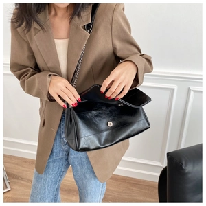 Detail of glossy black leather shoulder bag featuring vintage texture and silver magnetic clasp