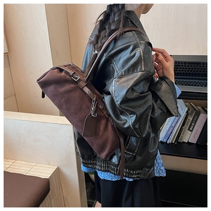 Detail of dark brown suede baguette bag with leather strap shown in a library setting