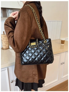 Close-up of black quilted chain bag featuring a gold rectangular metal swivel lock and strap
