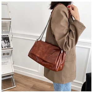 Detail of caramel brown leather shoulder bag with dark grey metal chain and side gussets