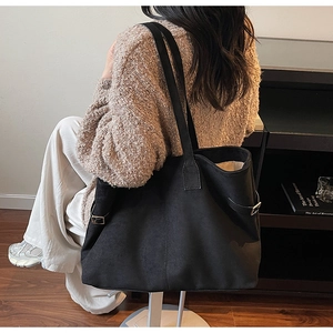 Side view of large black faux suede tote bag with metal buckle detail on shoulder strap