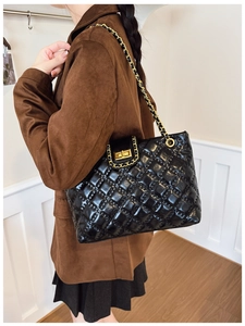 Detail of black quilted tote bag with gold chain strap shown on model's shoulder